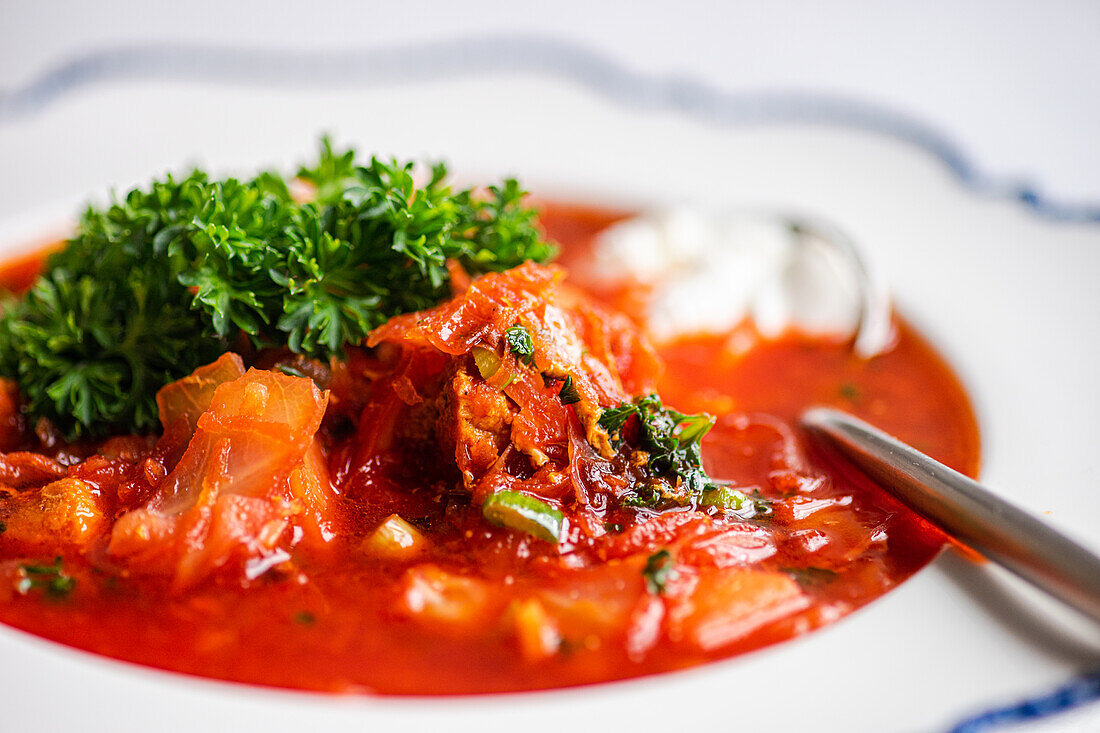 Close-up view of a bowl of hearty Ukrainian beetroot soup, known as borscht, garnished with parsley and a dollop of sour cream, ready to be enjoyed