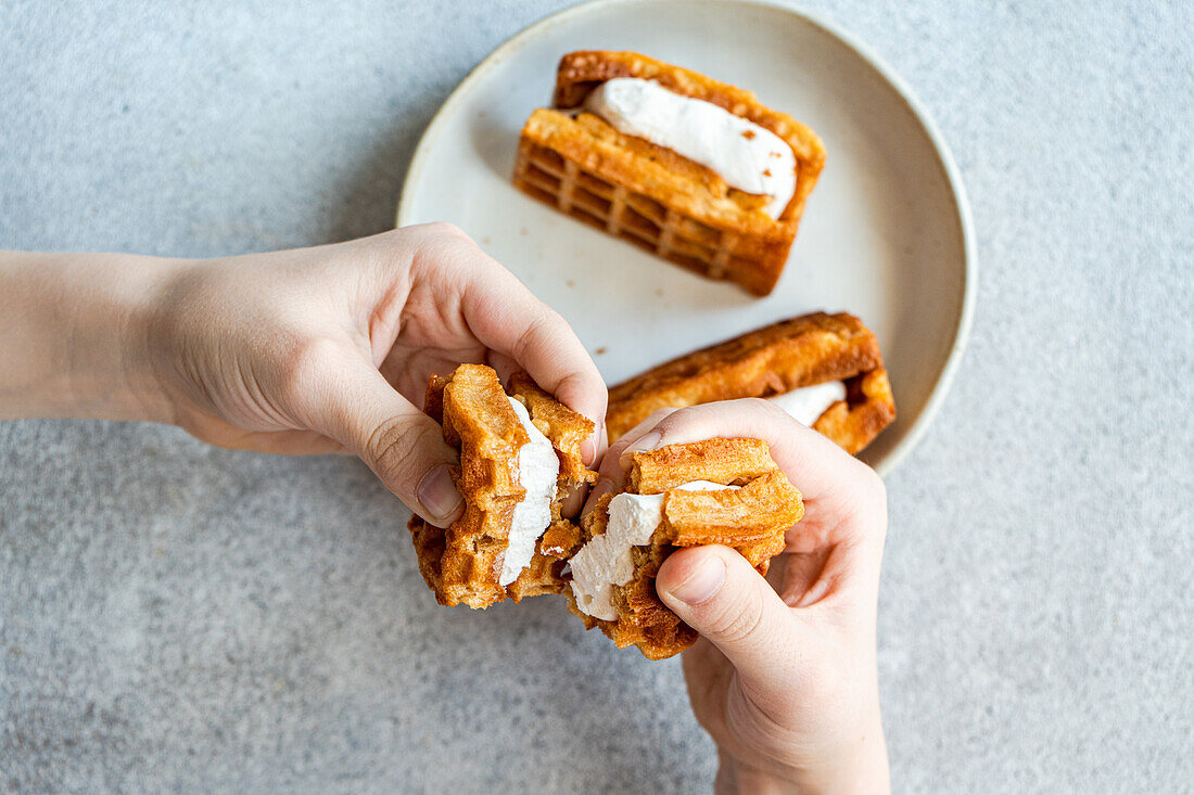 Hände halten leckere hausgemachte Waffeln mit cremiger Vanille-Marshmallow-Füllung, auf grauem Hintergrund