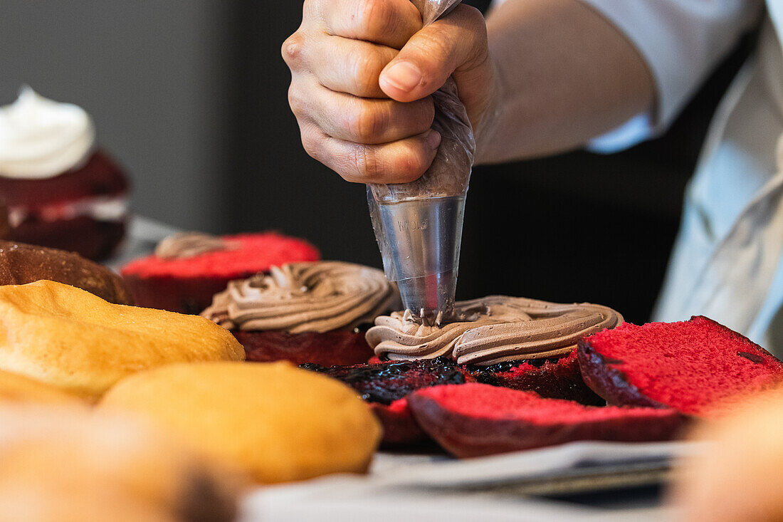 Crop anonymous cook with pastry bag adding chocolate cream on vegan sponge cakes while preparing desserts in bakehouse