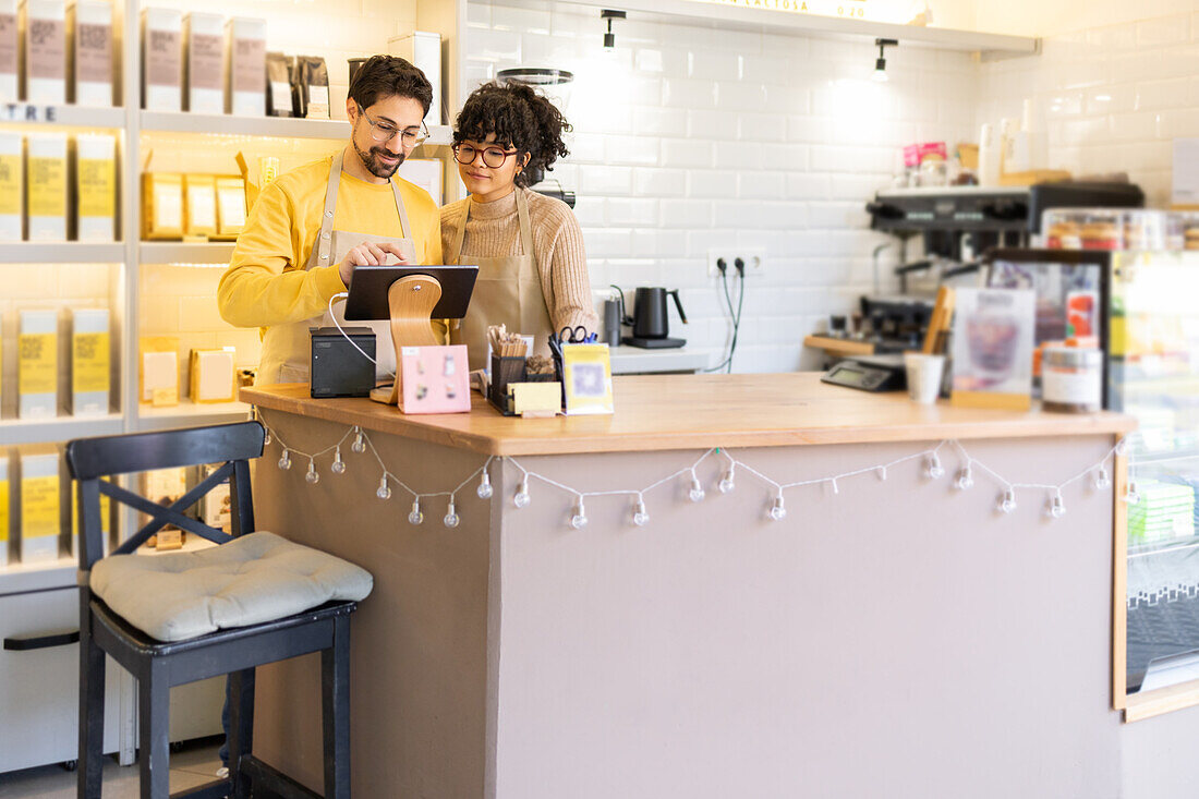 Two young multiethnic entrepreneurs are working collaboratively behind the counter in a warm and inviting cafe environment, illuminated with soft, natural light.