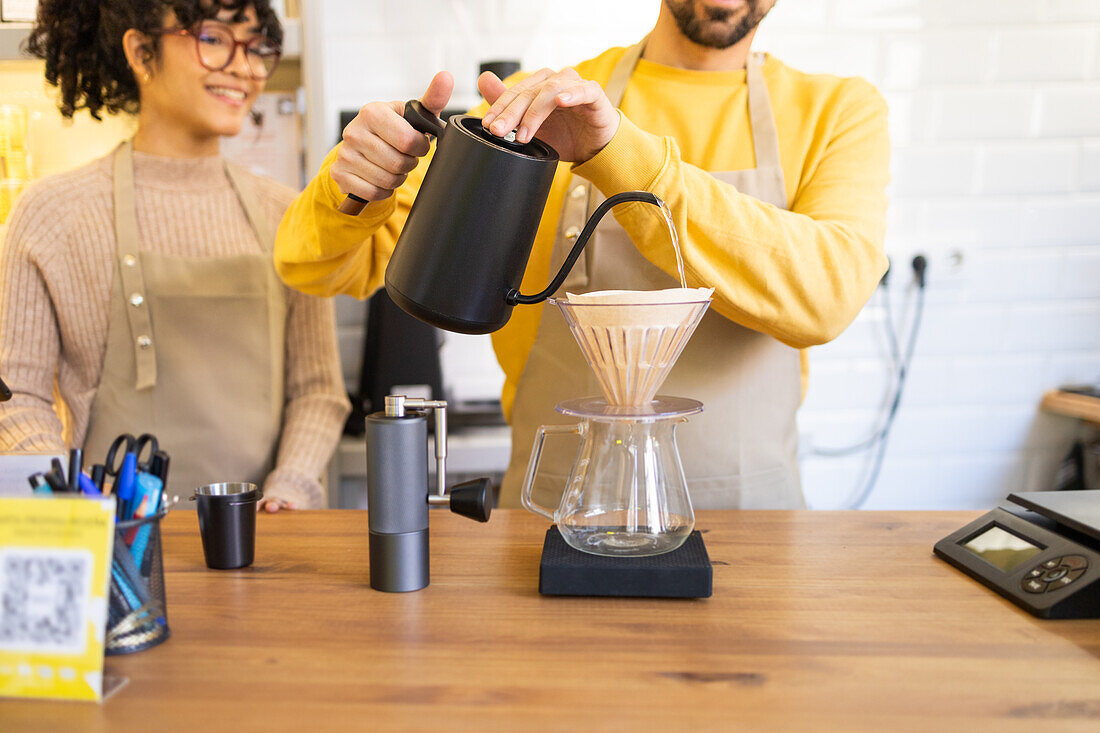 Barista carefully pours hot water into a coffee dripper over a carafe in a cozy cafe setting.