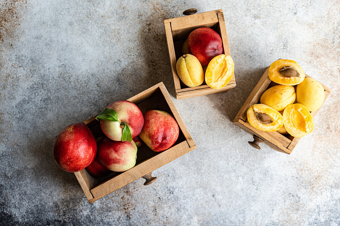 Top view whole and halved nectarines showcased in wooden crates, captured on a textured gray backdrop. The vibrant red skin and inviting yellow flesh highlight this seasonal fruit