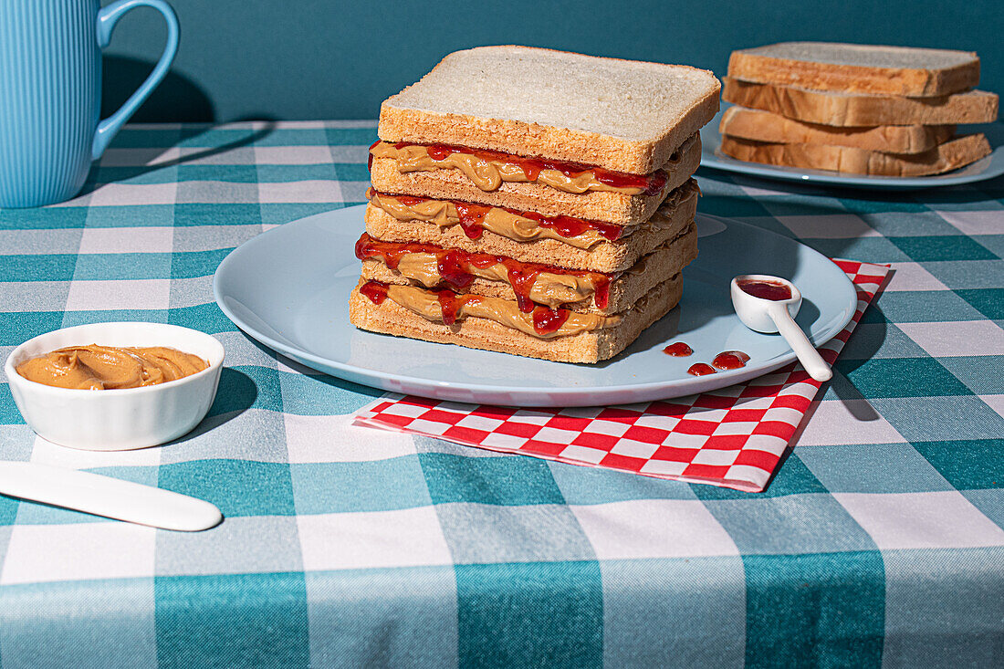 A delicious Peanut Butter and Jelly sandwich served on a blue plate , a blue cup of tea and some bread slices in a blue background