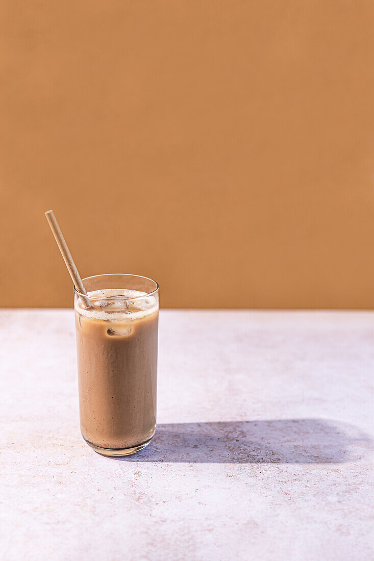 Eiskaffee in einem hohen Glas mit Strohhalm vor einem warmtonigen Hintergrund, der eine entspannte Sommeratmosphäre widerspiegelt