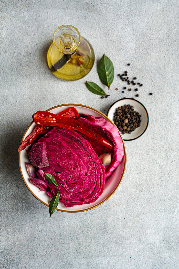 Eine farbenfrohe Schüssel mit fermentiertem Kohl, dazu Rote Bete, scharfer roter Pfeffer und Knoblauchzehen, akzentuiert mit Lorbeerblättern und schwarzem Pfeffer.