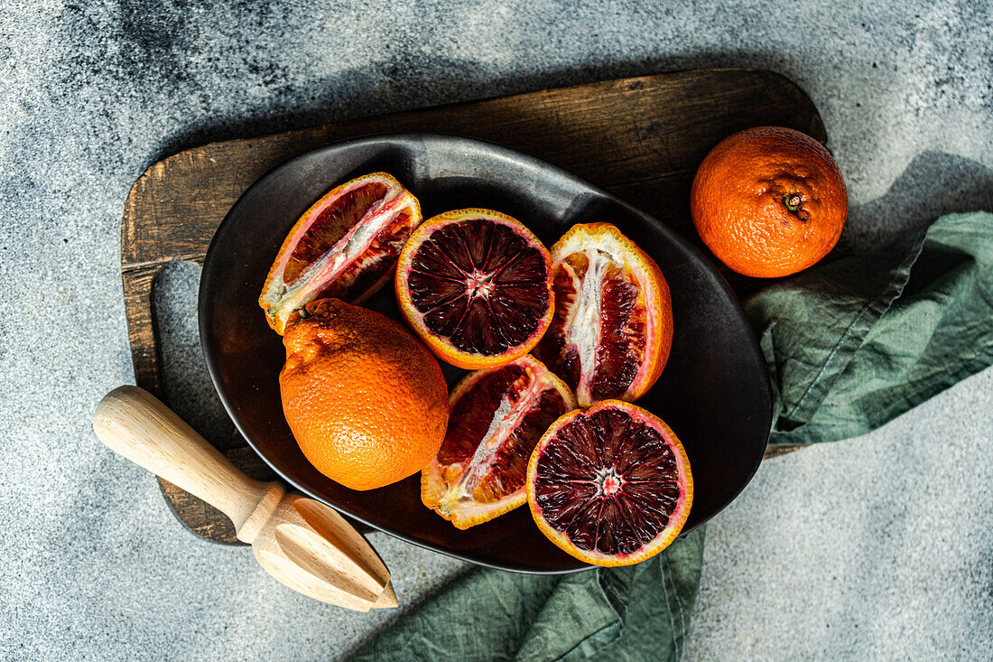 A top view of juicy blood oranges, freshly cut and displayed on a dark plate with a rustic wooden board background