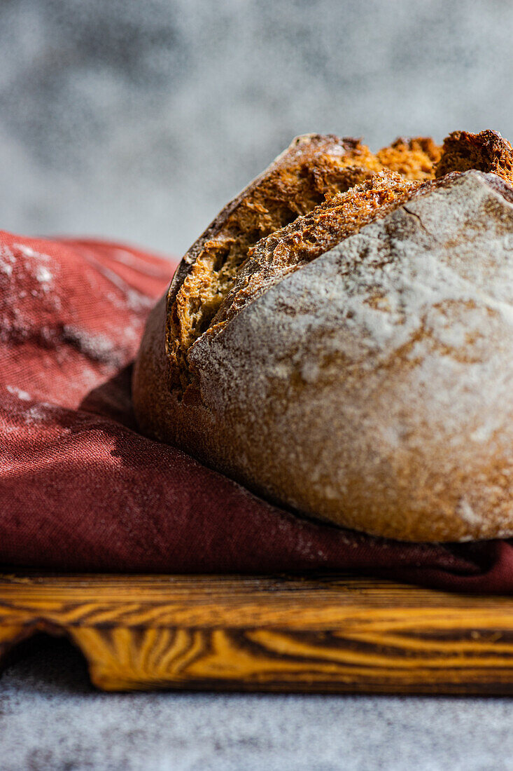 Handwerklich hergestelltes Sauerteigbrot aus Roggenmehl, ausgestellt auf einem hölzernen Schneidebrett mit einem roten Stoffhintergrund