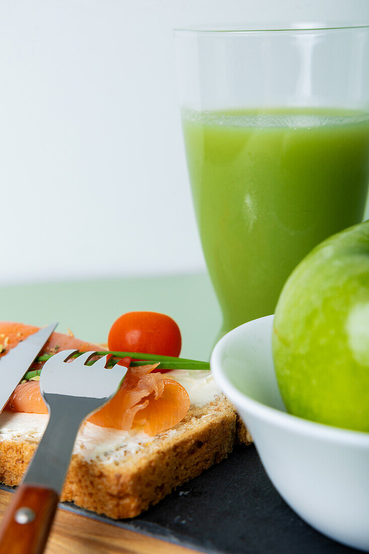 Erfrischende Auslage für gesunde Ernährung mit grünem Gurken- und Apfelsaft, geräuchertem Lachs auf Vollkorntoast, einem knackigen Apfel und Kirschtomaten.