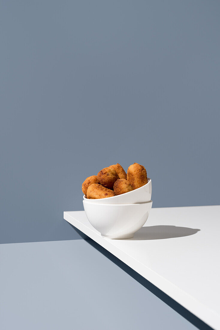 Spanische Vorspeisenkroketten in einer halbgefüllten weißen Schale vor einem grauen Hintergrund, die ein minimalistisches und modernes Food-Styling zeigt