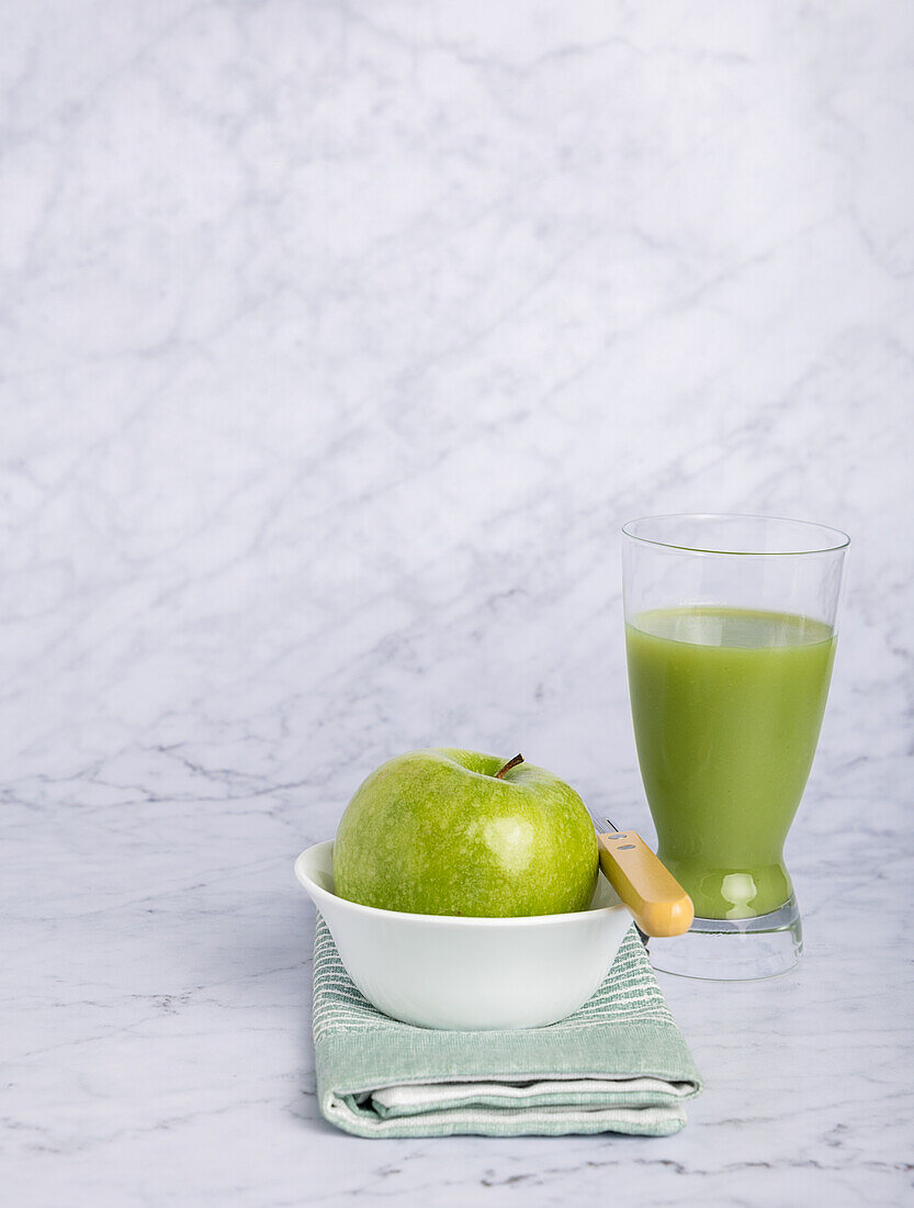 Green apple and a glass of cucumber and apple juice set on a marble surface. Simple and clean, this image conveys healthy eating and minimalist food presentation. Vibrant food items like the fresh apple and nutritious cucumber and apple juice