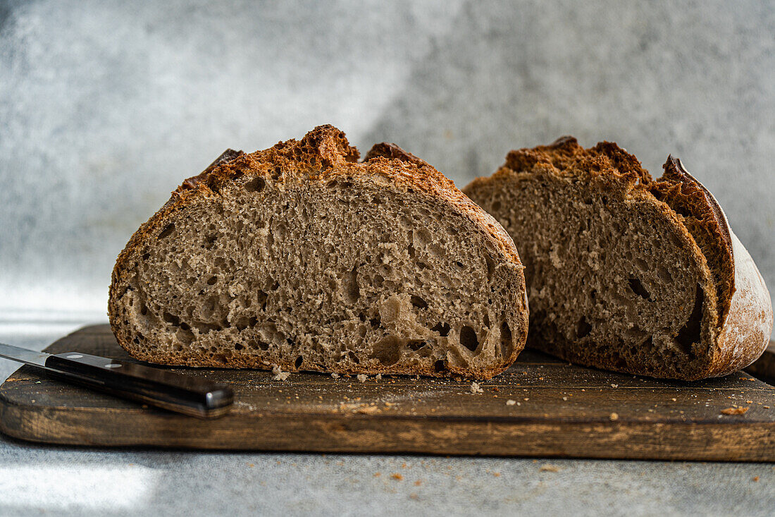 Ein frisch geschnittener Laib hausgemachtes Roggensauerteigbrot liegt auf einem rustikalen Schneidebrett aus Holz und präsentiert seine luftige Textur und Kruste