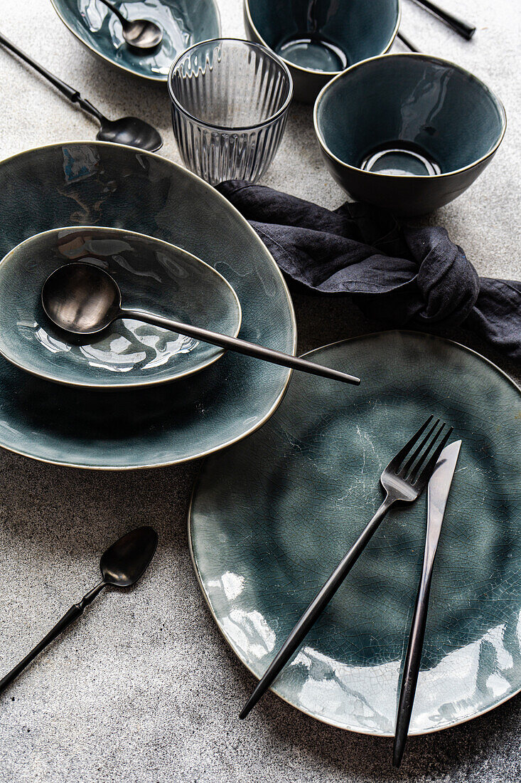 Top view of elegant table setting with green ceramic dishes, modern cutlery, and a dark napkin on a textured grey background. Ideal for sophisticated dining concepts.