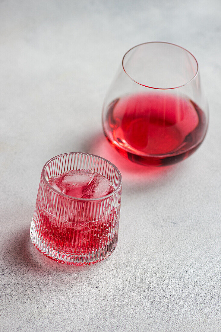 From above elegant glasses with a refreshing cherry vodka and tonic cocktail, garnished with ice cubes on a textured surface.