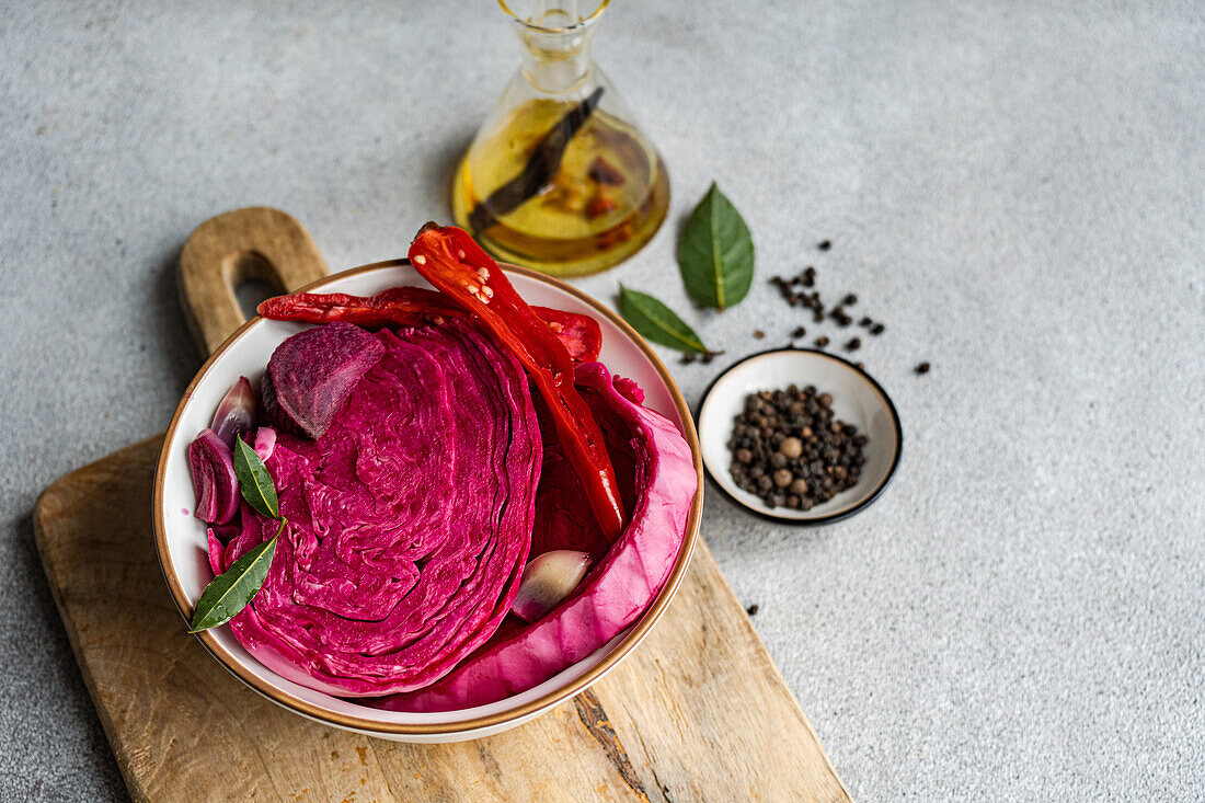 A vibrant bowl of fermented cabbage with slices of beetroot, spicy red pepper, and garlic, on a wooden board with olive oil and spices.