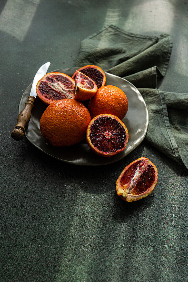 Fresh blood oranges on a dark plate with rustic knife and green cloth