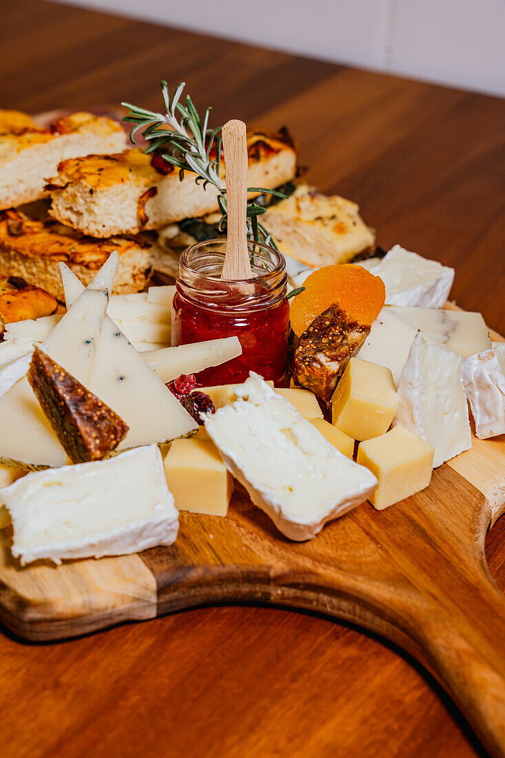 A rustic and inviting cheese platter featuring a selection of fine cheeses, crackers, and a jar of sweet jam, adorned with fresh rosemary