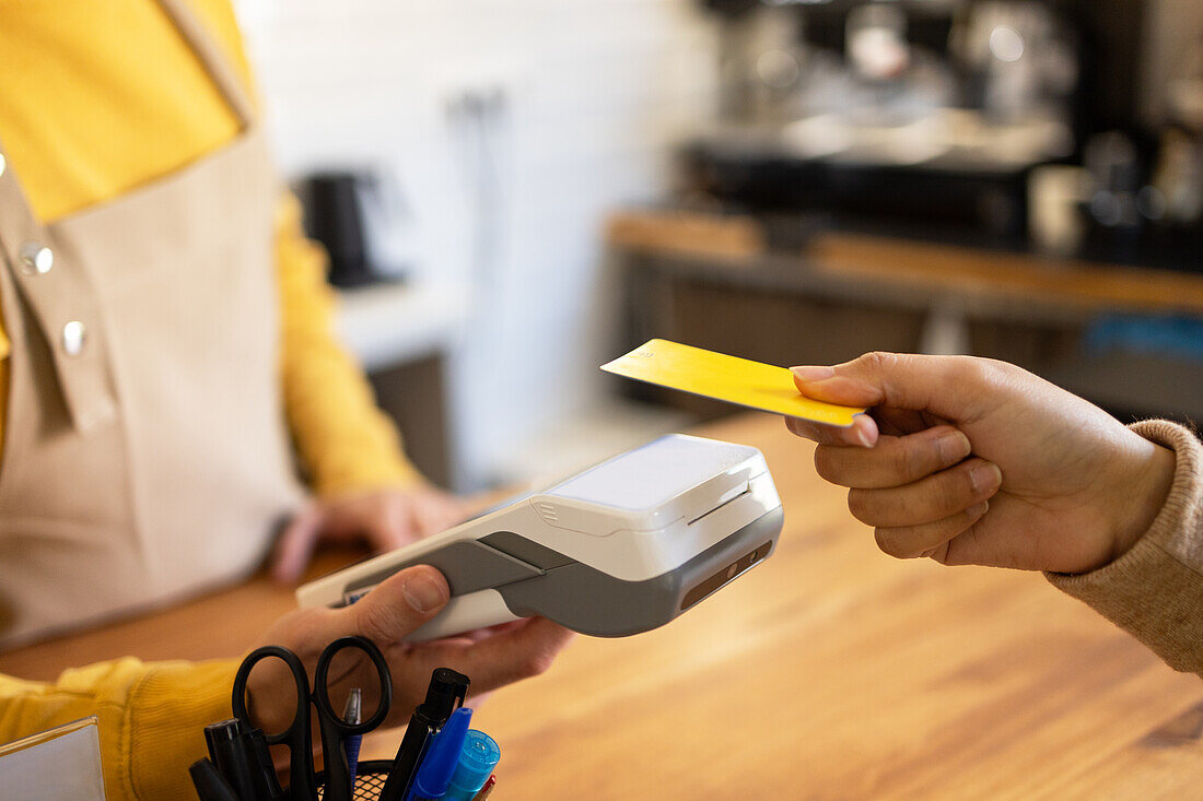 A customer makes a contactless card payment at a cafe's point of sale terminal, emphasizing convenience and technology.