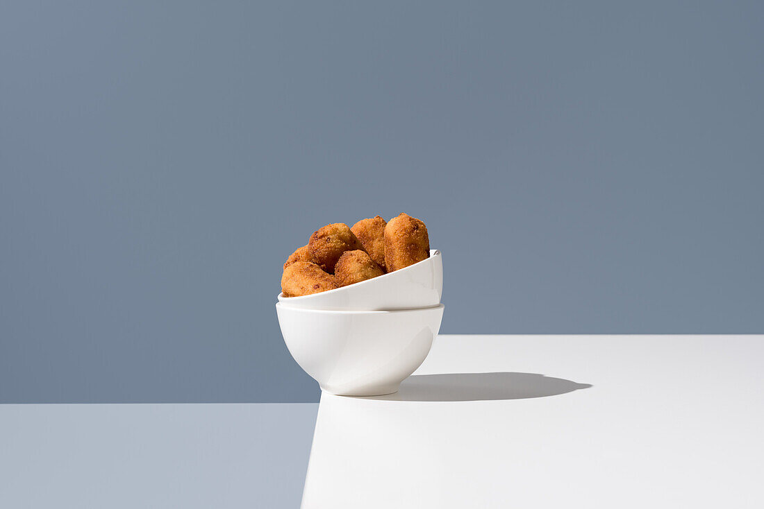 Spanish appetizer croquettes presented in a half-filled white bowl against a grey background, showcasing a minimalist and modern food styling