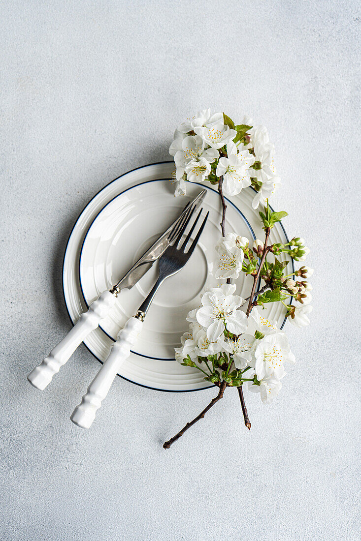 Elegant gedeckter Tisch mit weißen Kirschblüten auf einem Stapel von Tellern mit Silberbesteck daneben