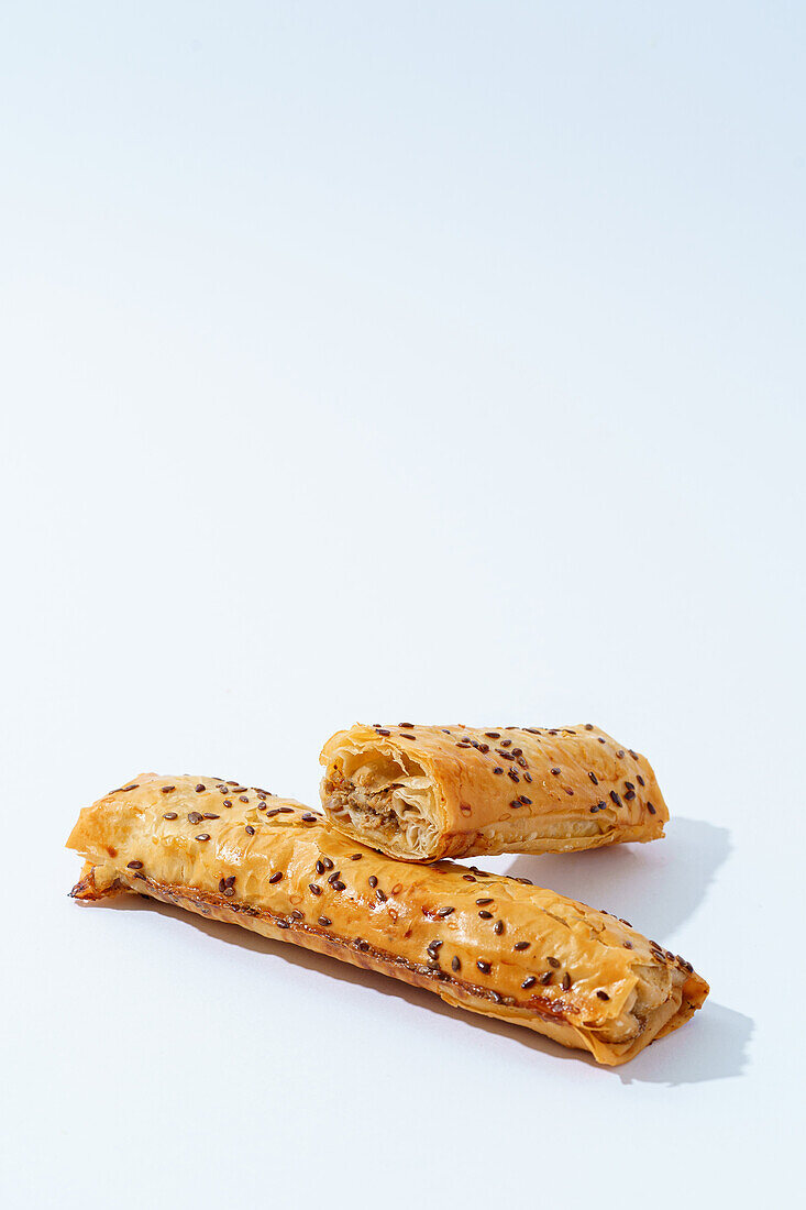 Zwei Stücke goldbrauner Kalbfleischblätterteig mit Leinsamen, frisch gebacken und vor einem weißen Hintergrund.