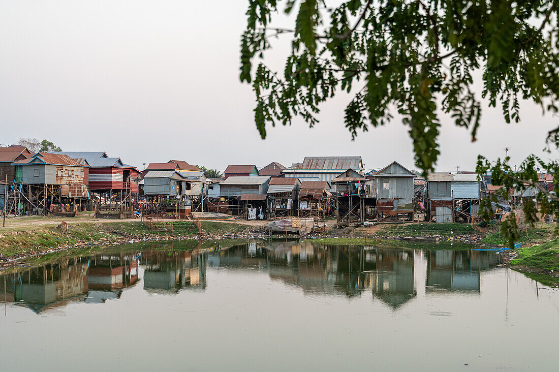 Stilt homes built on the riverbank, reflecting cultural architecture in a small, serene Cambodian village.