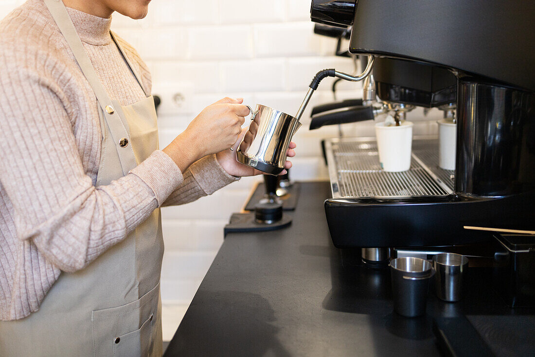 A focused barista using a modern espresso machine to steam milk in a metal pitcher, preparing for a creamy coffee drink.