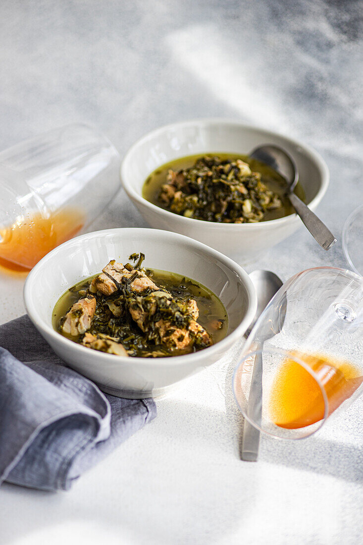 A Georgian culinary delight, this photo features a traditional spring stew made with succulent meat, aromatic white wine, tart green plums, and a blend of fresh herbs including tarragon, coriander, parsley, and spring onions, all beautifully presented in bowls.