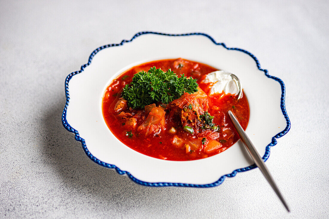 Vibrant bowl of Ukrainian borsch topped with fresh parsley and a dollop of sour cream, presented elegantly on a blue-trimmed white plate