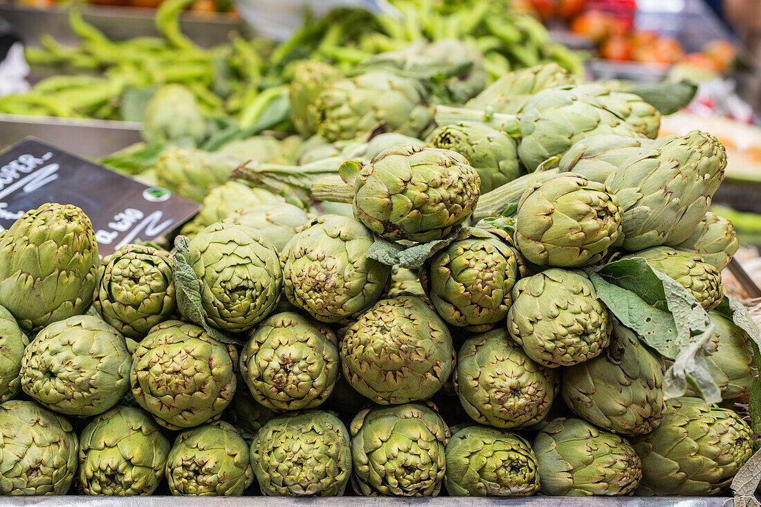 Bunch of fresh green artichokes for sale at a local farmers market with a price sign