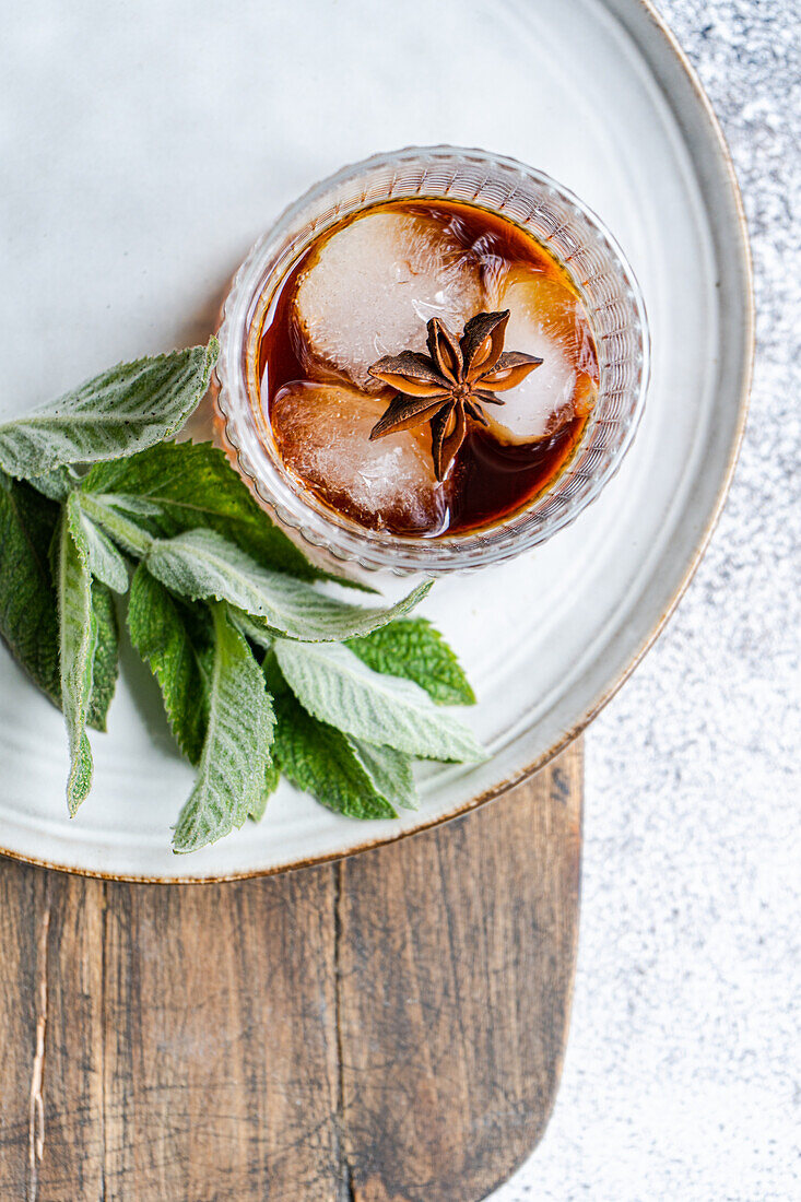 Top view of a refreshing cherry cocktail with ice cubes and a sprig of mint, garnished with a star anise on a wooden table.