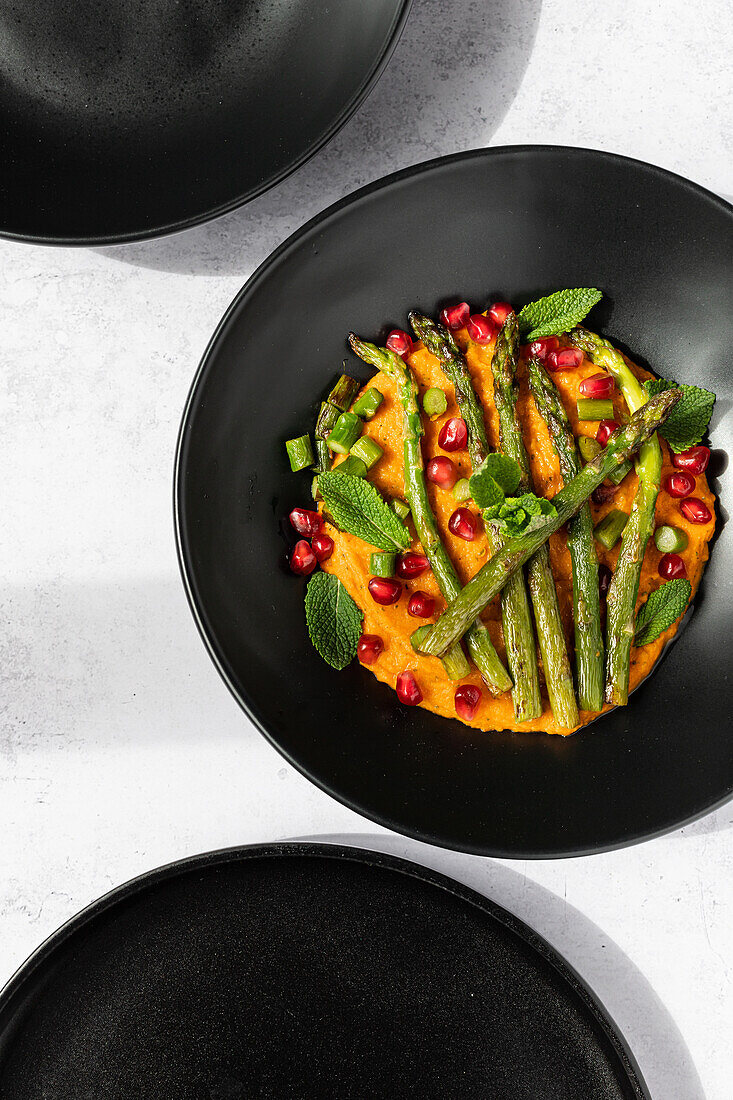 From above gourmet dish of grilled asparagus and mashed sweet potato garnished with pomegranate and mint, shot from above.