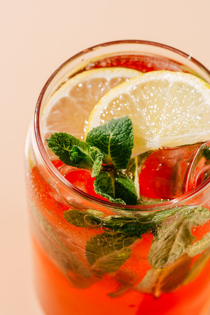 Vibrant berry-orange lemonade garnished with fresh mint leaves and lemon slices, served in a glass with ice; perfect for a hot day.