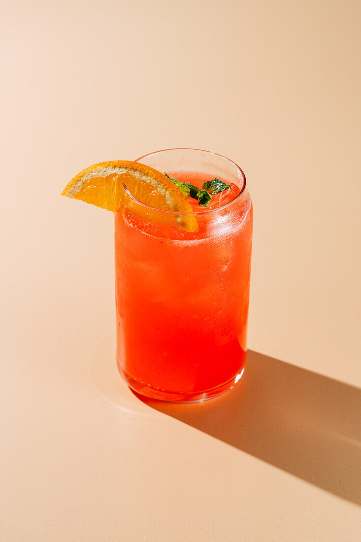 A vibrant glass of berry-orange lemonade garnished with a fresh orange slice and mint, served cold with ice on a neutral background.