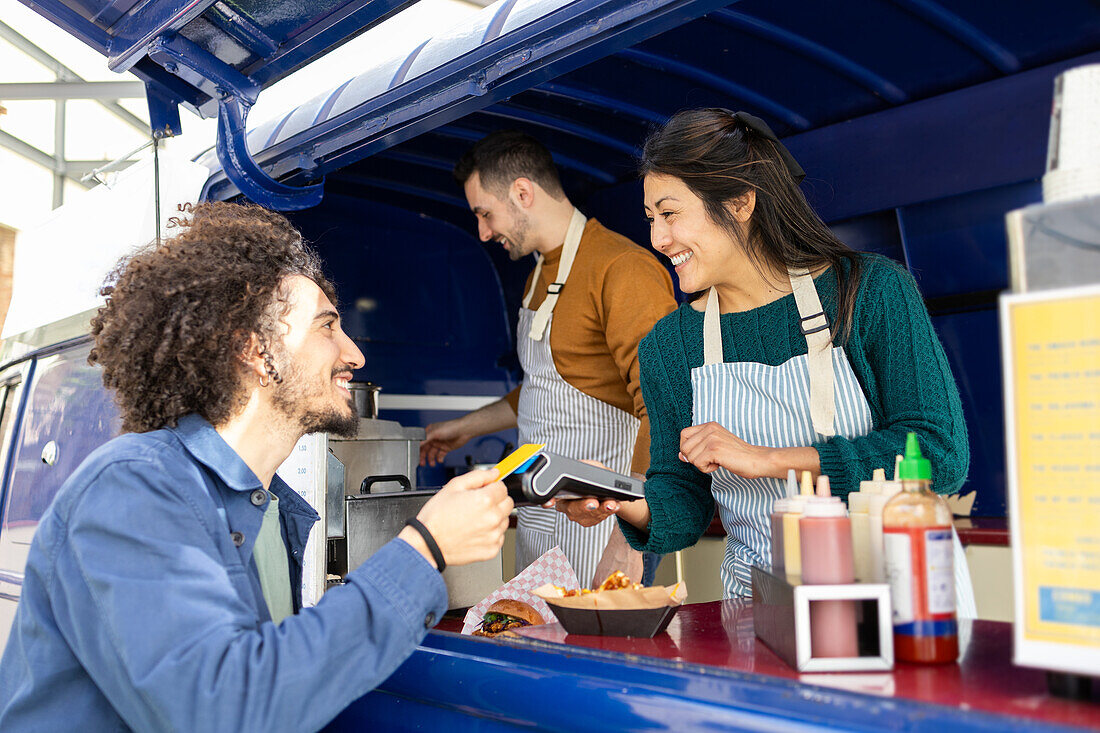 A cheerful customer pays with a card at a vibrant food truck while engaging with friendly staff