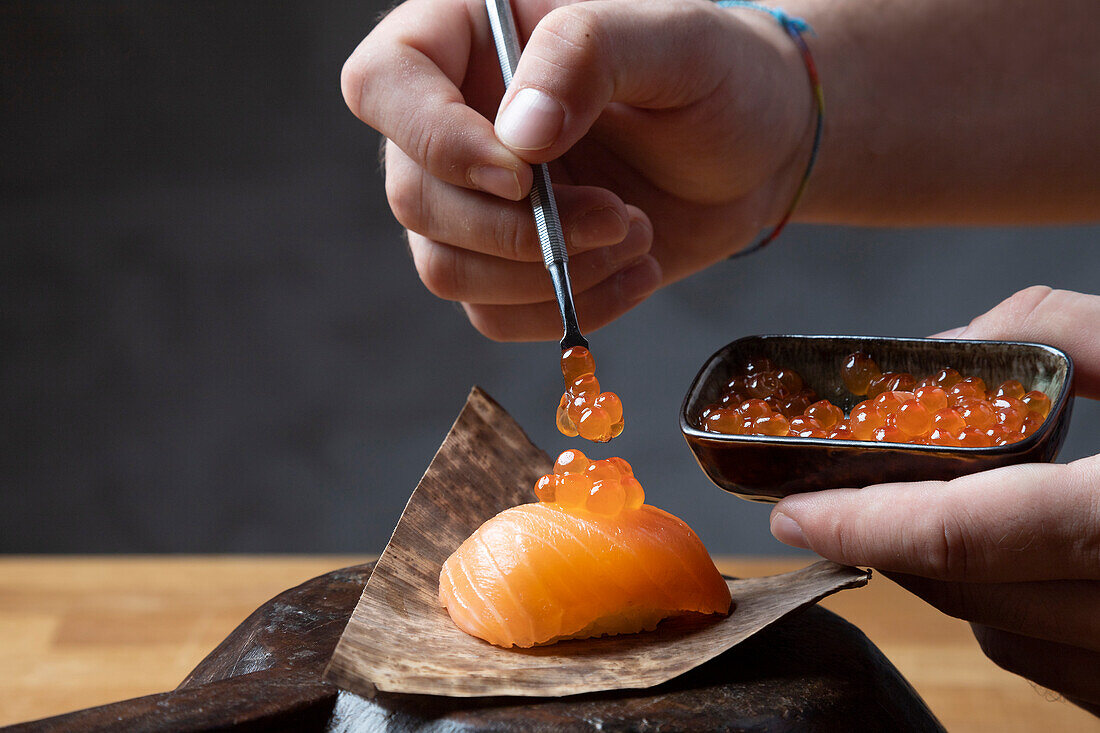 A detailed depiction of a chef skillfully adding salmon roe to a sushi dish using precision tweezers, emphasizing the art of sushi preparation