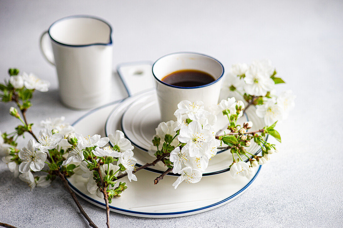 Elegant gedeckter Tisch mit weißen Kirschblüten und einer Tasse Kaffee vor einem ruhigen Hintergrund