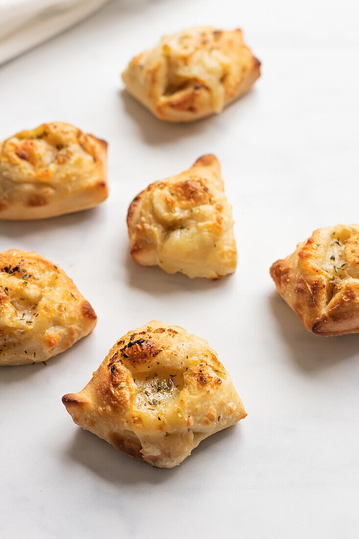 Eine Auswahl goldener Knoblauchbrotknoten, frisch gebacken und mit geschmolzenem Käse überbacken, fein säuberlich auf einer weißen Fläche angeordnet.