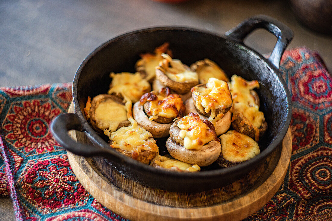 Mushrooms stuffed with melted sulguni cheese, baked and served in a rustic black skillet, placed on a colorful textile