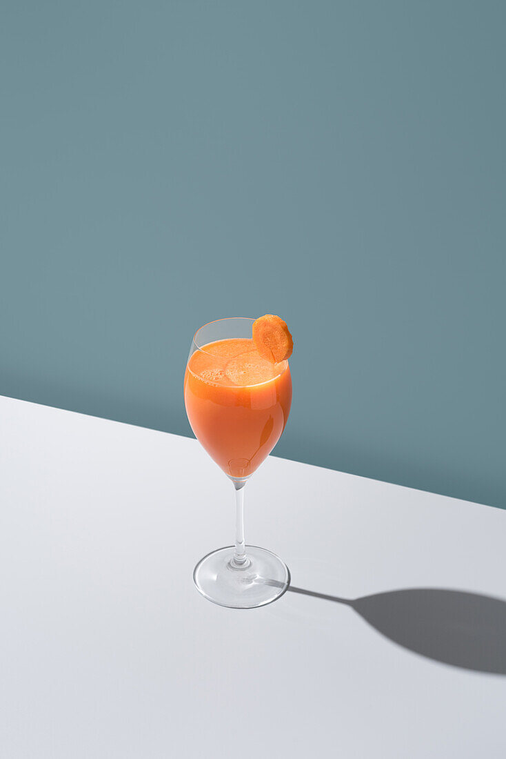 A refreshing glass of orange juice garnished with a slice, casting a shadow on a white surface.