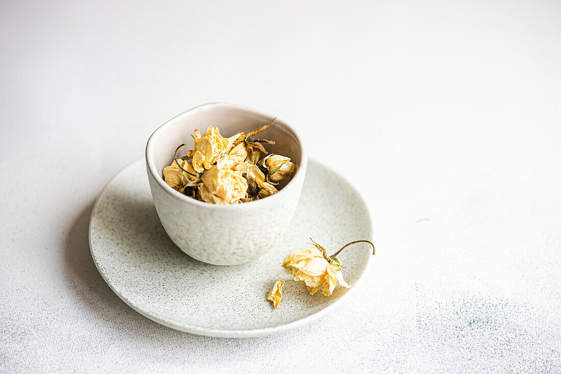 A tasteful arrangement of dried roses nestled in a textured ceramic bowl and plate, set against a soft white background