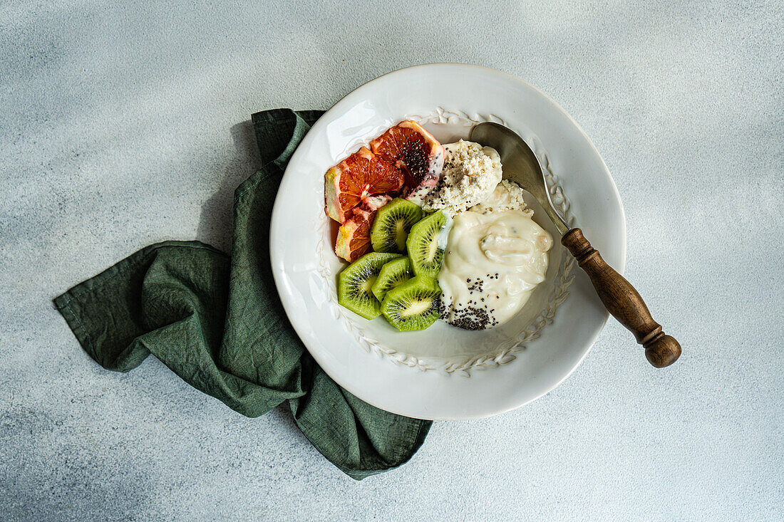 Blick von oben auf eine gesunde Schüssel mit Naturjoghurt, Hüttenkäse, Chiasamen und frisch geschnittener Kiwi und sizilianischer Orange für einen guten Start in den Tag