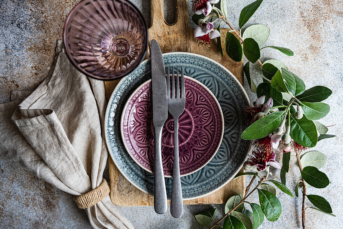 Top view beautifully arranged dining table featuring Feijoa accents, with detailed ceramic dishware in purple and grey tones Exotic Feijoa flowers and leaves add a unique touch to the rustic background, enhancing the meal's ambiance