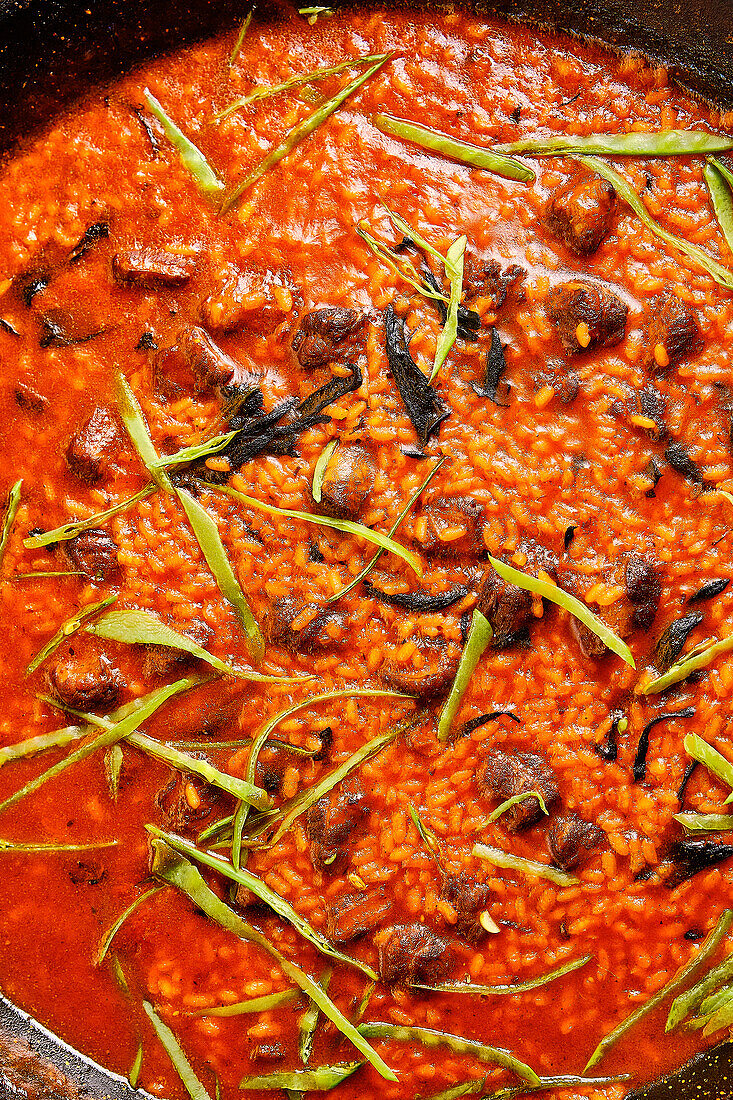 Close-up of a delicious risotto adorned with slender green garnish in a rustic skillet, ready to serve.