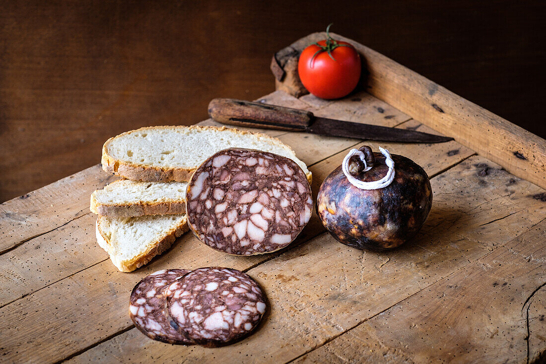 Aufgeschnittene Wurstwaren, möglicherweise Salami, und rustikale Brotscheiben, die auf einem Holzbrett präsentiert werden, um ein traditionelles und appetitliches Ambiente zu schaffen.