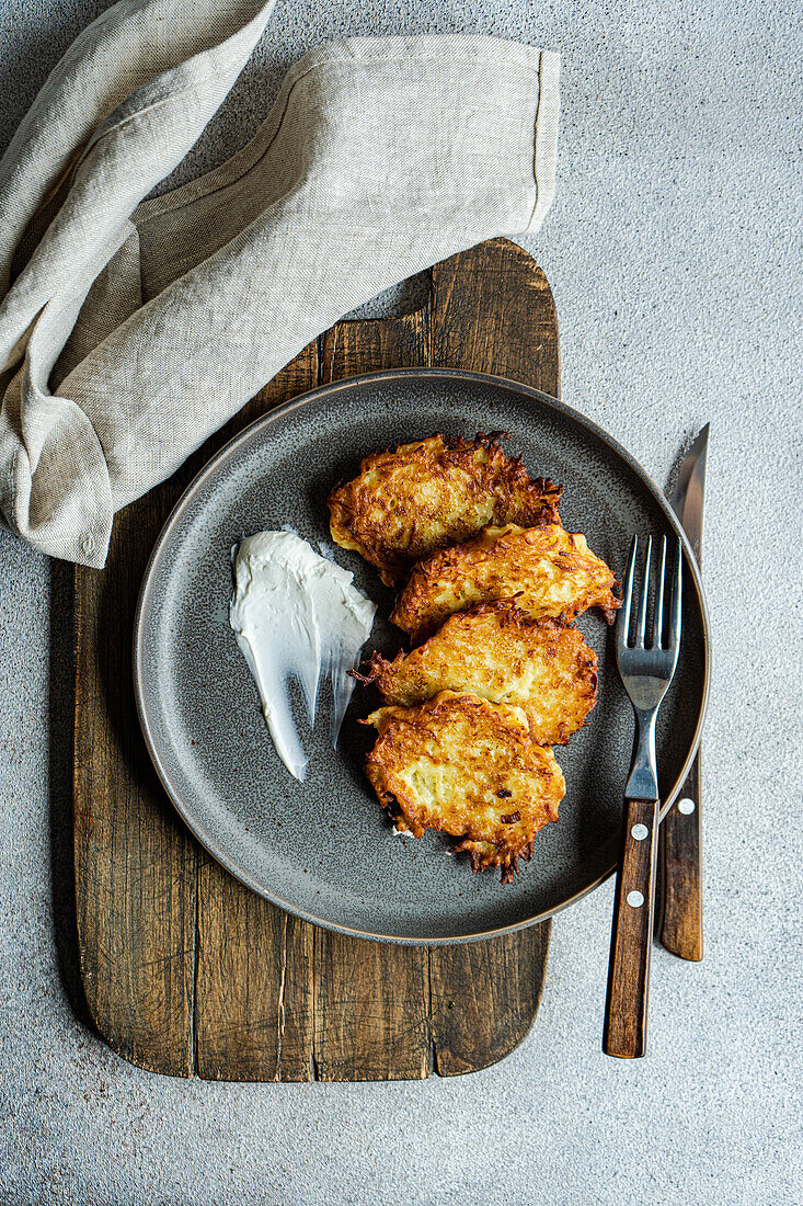 Overhead view of savory potato american pancakes served with sour cream on a rustic plate, perfect for traditional cuisine.