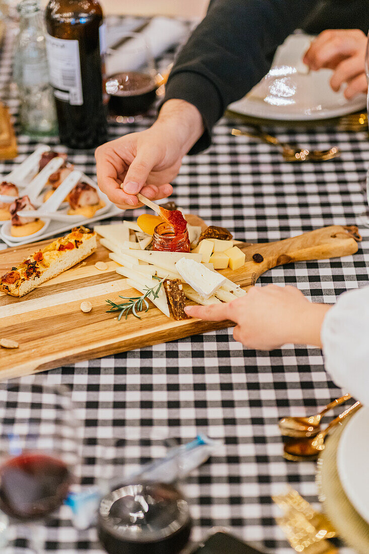 Anonyme Hände von Gästen, die bei einer stilvollen Dinnerparty von einer hölzernen Käseplatte mit verschiedenen Käsesorten und Focaccia auswählen