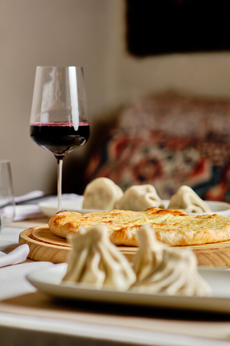 Ein traditionelles georgisches Festmahl mit Khachapuri und Khinkali, perfekt gepaart mit einem Glas Rotwein, vor einem sanft verschwommenen Hintergrund, der die gemütliche Atmosphäre betont