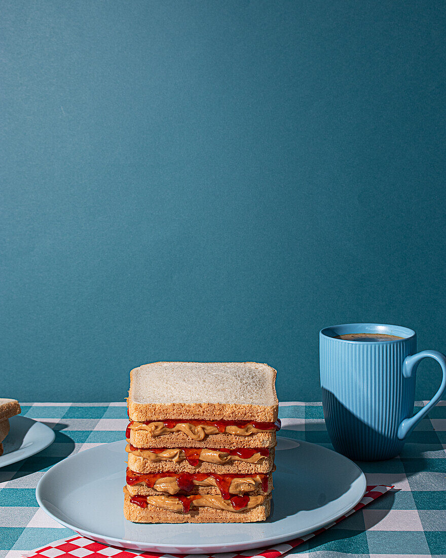 Leckere Erdnussbutter- und Gelee-Sandwiches auf einem blauen Teller, mit einer Tasse amerikanischen Kaffees und einigen Brotscheiben in einem blauen Hintergrund