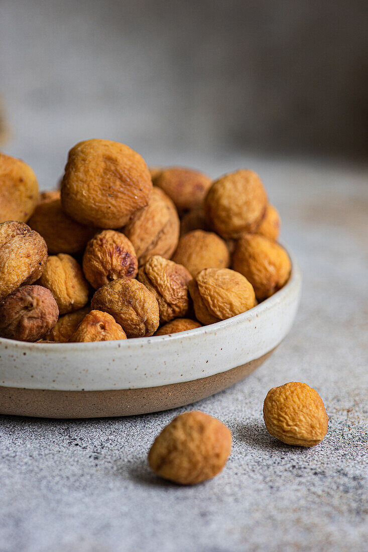 A bowl of Arashan Kandak, Central Asian wild apricots sun-dried for a healthy snack, set on a textured surface with a rustic background