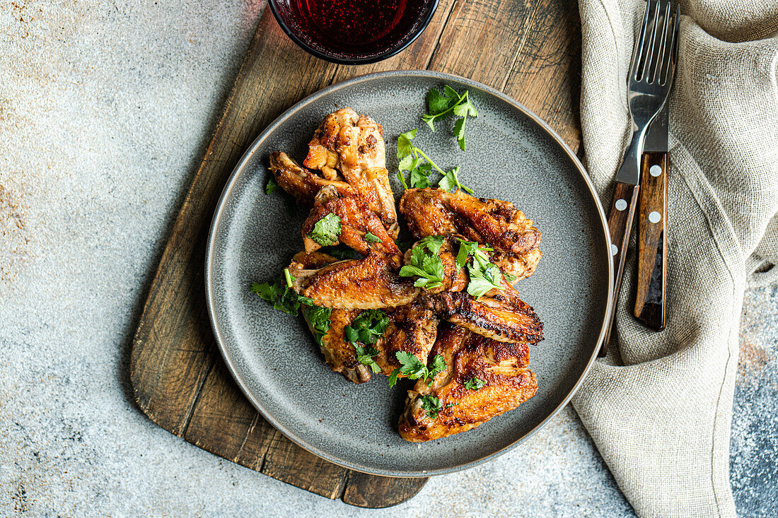 Top view succulent roasted chicken wings coated in a spicy sauce, garnished with fresh coriander leaves, presented elegantly on a plate beside a refreshing cherry cocktail.